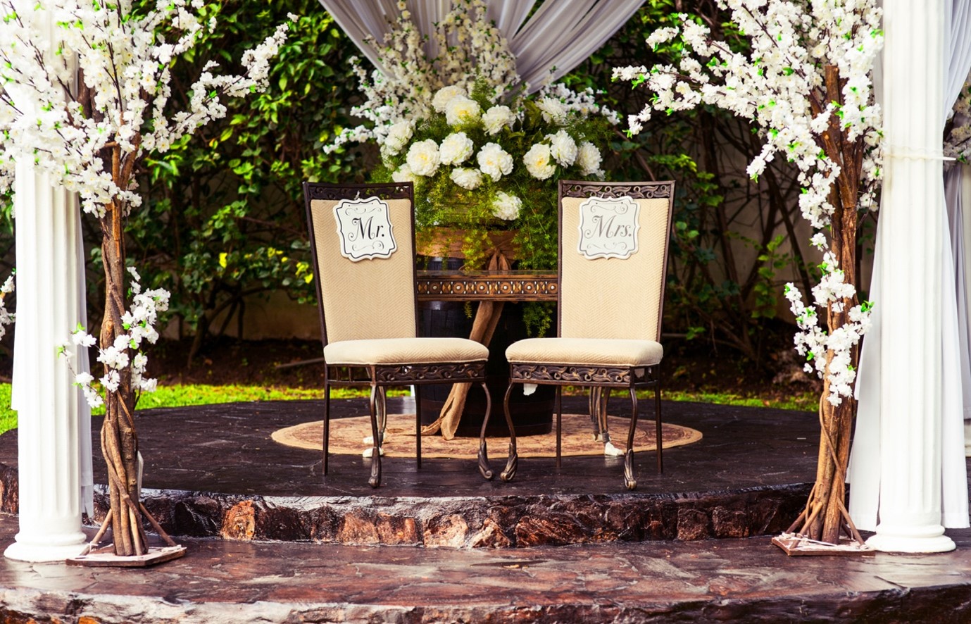 A Stage at a Spring Wedding Featuring Two Chairs for the Bride and Groom and Lots of Floral Arrangements